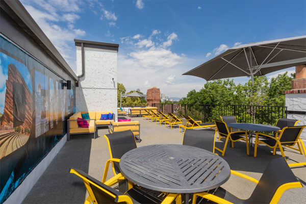 Rooftop patio with tables, lounge chairs, and mural overlooking Denver.
