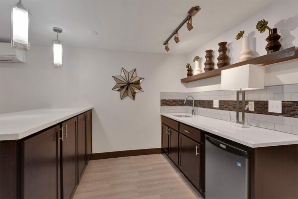 Demo kitchen with wood floor and cabinets, white counters, eclectic decor, and pendant lights.