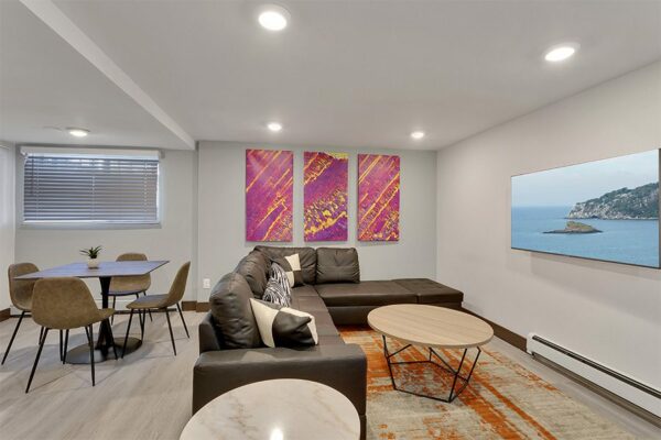 Lounge with wood floor, dining tables, plush sectional, and large TV.