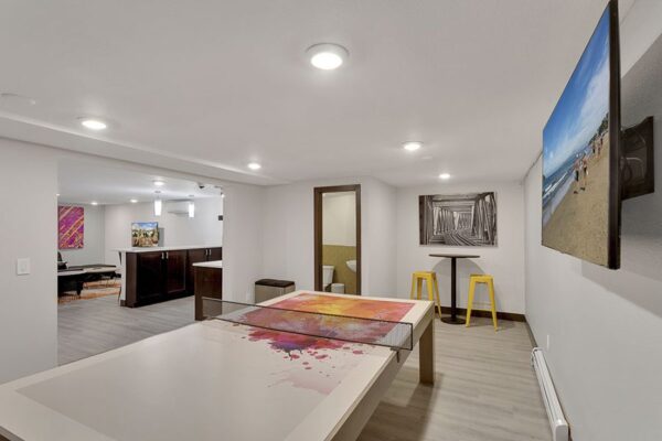 Clubroom with wood floor, table tennis, bar tables with stools, and wall mounted TV.