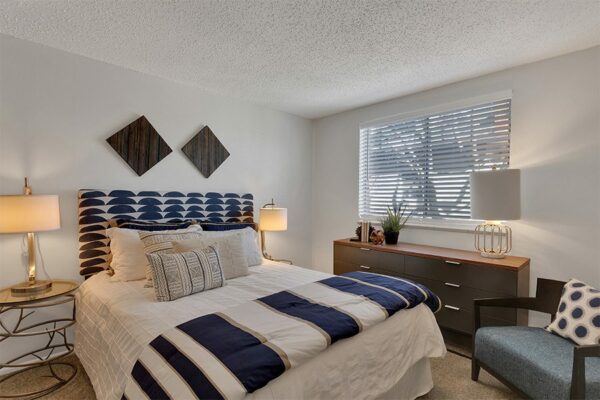 Bedroom with plush bed, bedside tables with lamps, wood dresser, and large window.