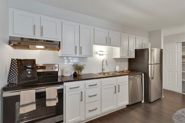 Kitchen with wood floor, white cabinets, dark counters, and stainless steel appliances.