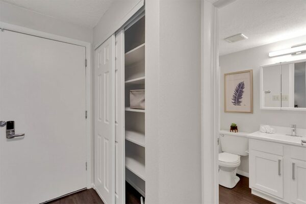 Bathroom with white cabinets, framed mirror, and closet with shelves.