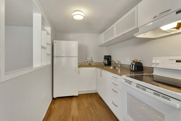 Apartment kitchen with wood floor, white cabinets, and white appliances.