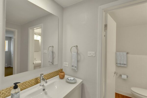 Bathroom with white counter, tiled backsplash, and large mirror.