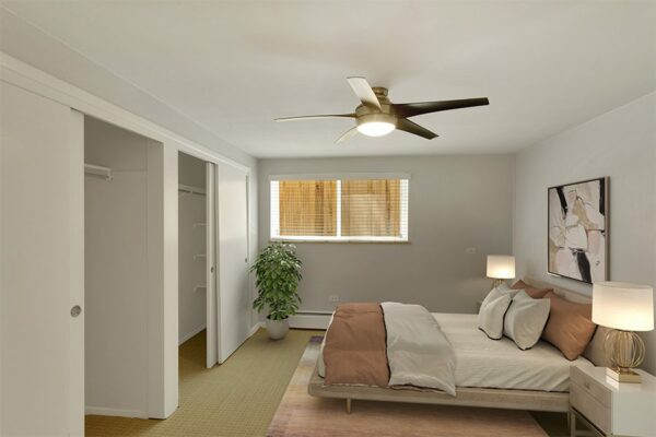 Apartment bedroom with plush bed, framed artwork, and ceiling fan.