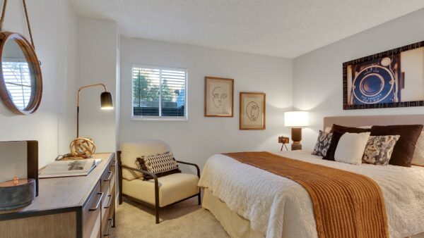 Bedroom with plush bed, wood dresser, framed artwork, and lounge chair.