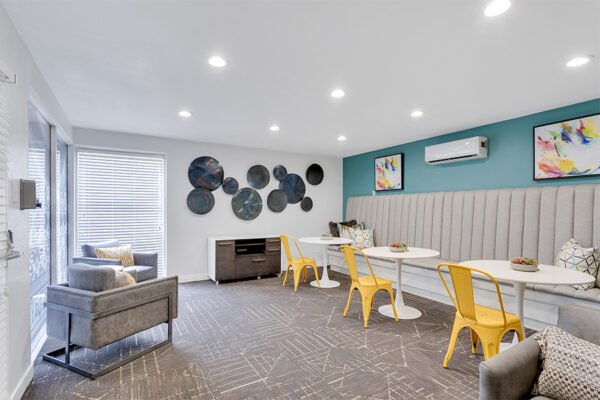 Lounge area with plush booth seats and tables, potted tree, and wall art.