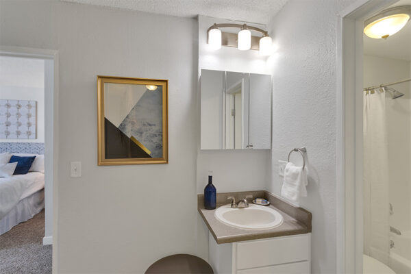 Bathroom with white cabinets, triple mirror medicine cabinet, and wall art.