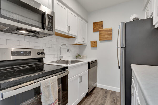Kitchen with wood floor, white cabinets, light counters, stainless steel appliances, and wood wall art.