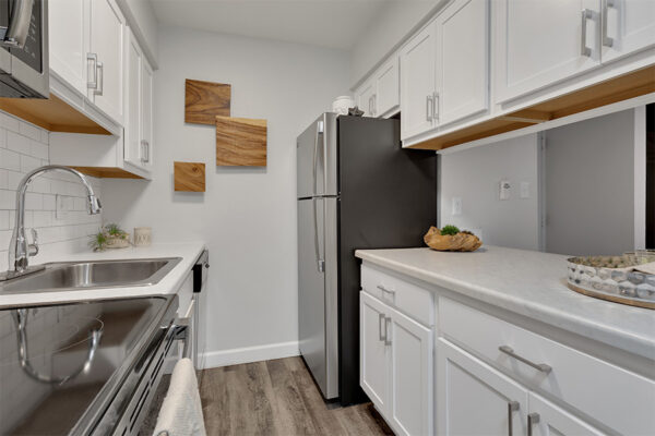 Kitchen with wood floor, white cabinets, light counters, stainless steel appliances, and wood wall art.