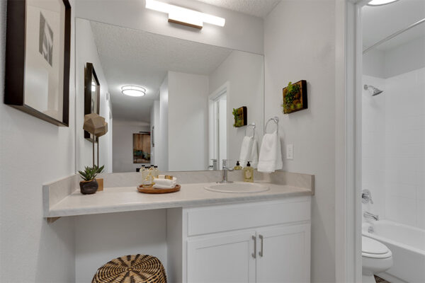 Bathroom with white cabinets, light counters, large mirror, and earthy wall decor.