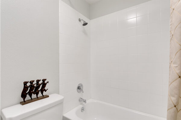 Bathroom with tiled shower tub with curtain and dog sculpture.