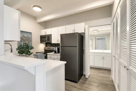 Kitchen with wood floor, white cabinets and counters, and gray appliances.