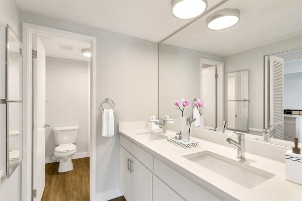 Bathroom with white cabinets and counters, large mirror, and bright lighting.