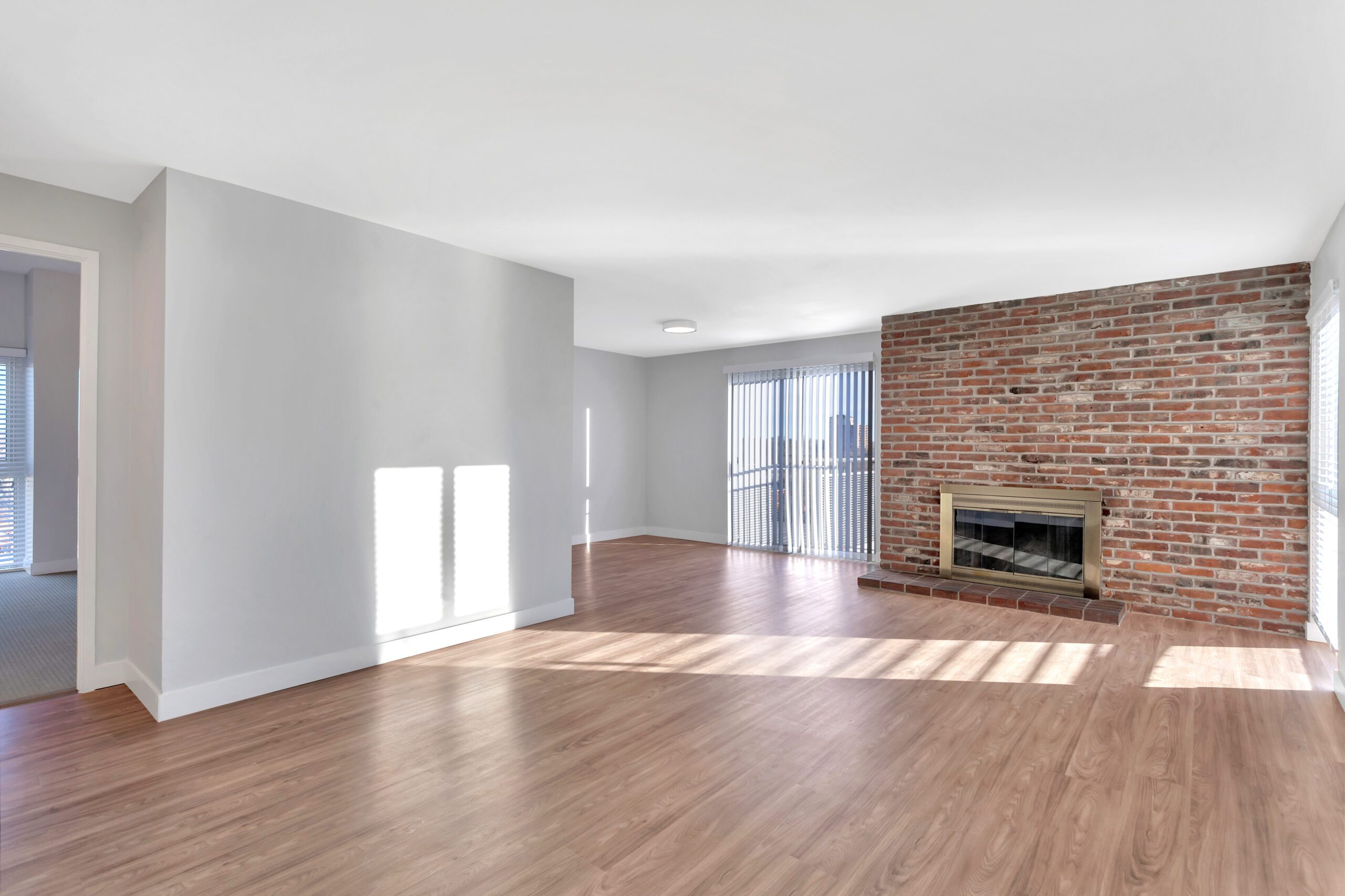 Living room with wood floor, brick accent wall with fireplace, and door to balcony.