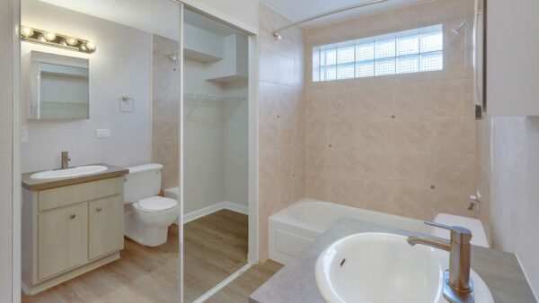 Bathroom with wood floor and cabinet, closet with mirror door, and tiled shower tub.