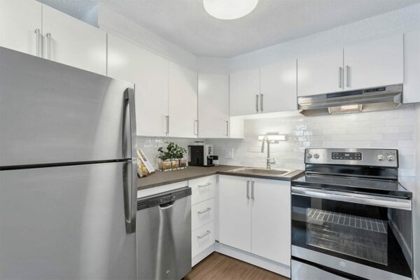 Apartment kitchen with wood floor, white cabinets, grey counter, and stainless steel appliances.