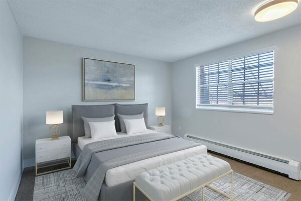 Apartment bedroom with plush bed, bedside tables with lamps, and large window.