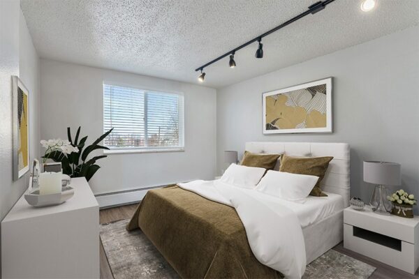 Apartment bedroom with plush bed, framed art, and large window.