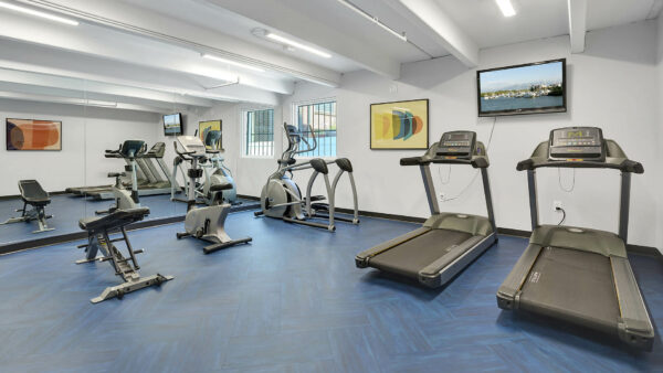 Fitness center with mirror wall, wall mounted TV, treadmills, elliptical, and exercise bike.