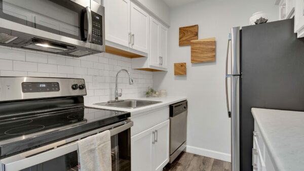 Kitchen with wood floor, white cabinets, light counters, stainless steel appliances, and wood wall art.