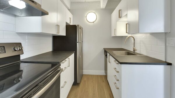 Kitchen with wood floor, white cabinets, dark counters, and stainless steel appliances.