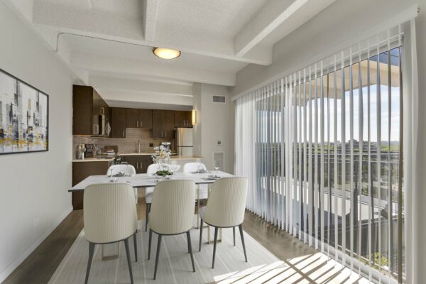 Dining room with modern table and chairs next to large bright window with blinds.