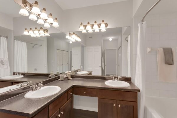Bathroom with wood cabinets, grey counter, large mirror, and tiled shower tub.