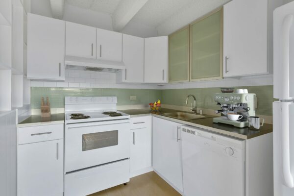 Kitchen with wood floor, white cabinets, green tiled backsplash, and white appliances.