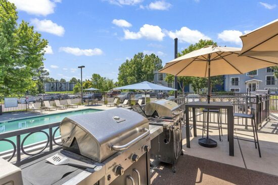 Outdoor BBQ area with grills, dining tables, and fenced pool.
