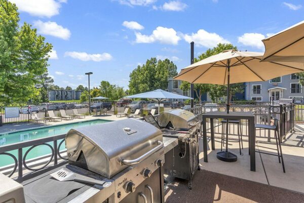 Outdoor BBQ area with grills, dining tables, and fenced pool.