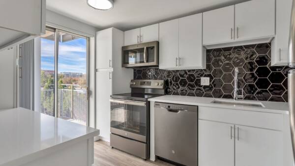 Kitchen with wood floor, white cabinets and counters, stainless steel appliances, and door to balcony.