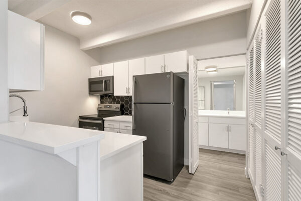 Kitchen with wood floor, white cabinets and counters, dark gray appliances, and bright lights.