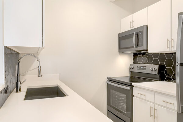 Kitchen with white cabinets and counters, dark gray appliances, and hexagon tiled backsplash.