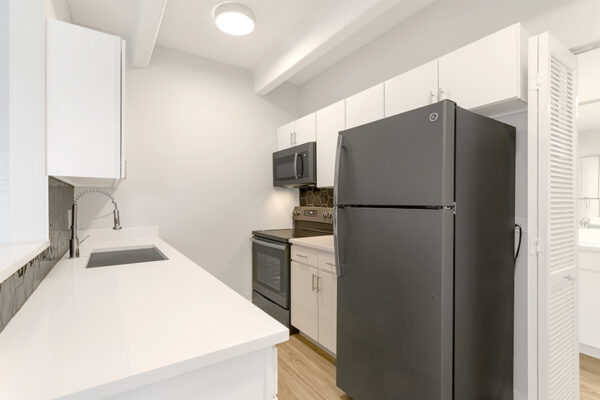 Kitchen with white cabinets and counters, dark grey appliances, and tiled backsplash.