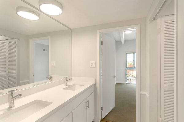 Bathroom with white cabinets and counters, large mirror, round light, and closet door.