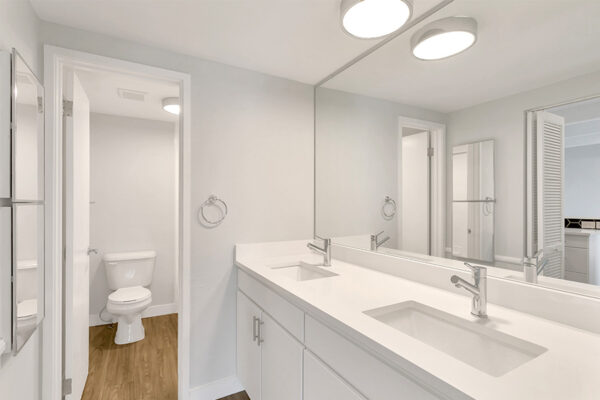 Bathroom with white cabinets and counters, large mirror, and round light.