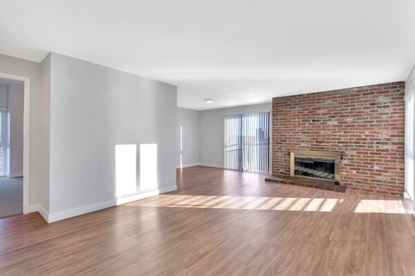 Living room with wood floor, brick accent wall with fireplace, and sliding door to balcony.