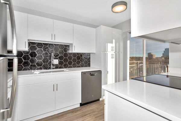 Kitchen with wood floor, white cabinets and counters, dark gray appliances, and hexagonal tiled backsplash.