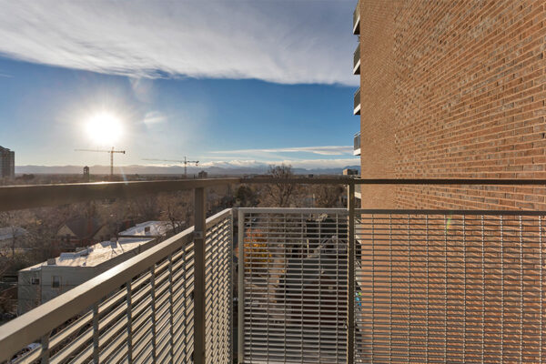 Balcony with metal railing overlooking Denver under setting sun.