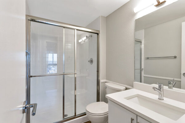 Bathroom with white cabinets and counters, glass wall shower, and bright lights.
