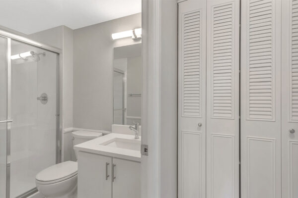 Bathroom with white cabinets and counter, large mirror, and glass shower door.