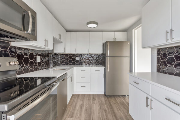 Kitchen with wood floor, white cabinets and counters, and stainless steel appliances.