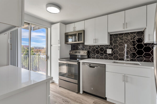 Kitchen with wood floor, white cabinets and counters, dark gray appliances, and sliding door to balcony.