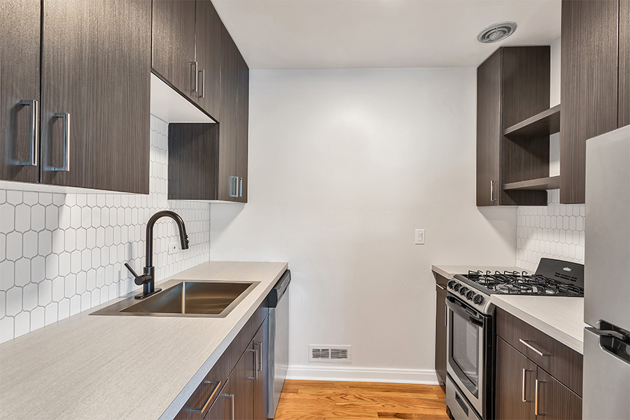 Kitchen with wood floor, dark cabinets, light counter, stainless steel appliances, and tiled backsplash.
