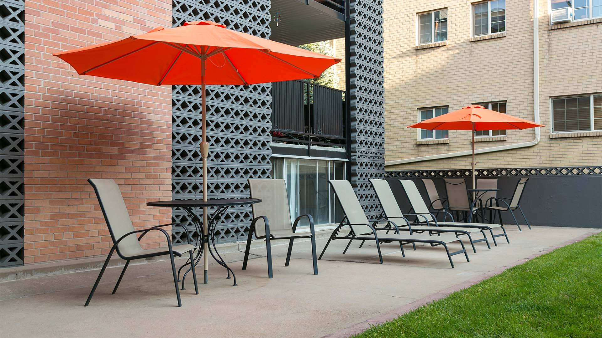 Patio with lounge chairs, dining tables, and umbrellas overlooked by apartment balconies.