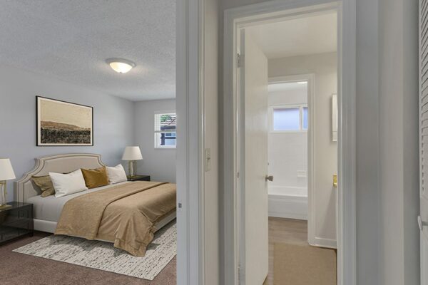 Bedroom with rug, bed with plush headboard, artwork, bathroom and window.