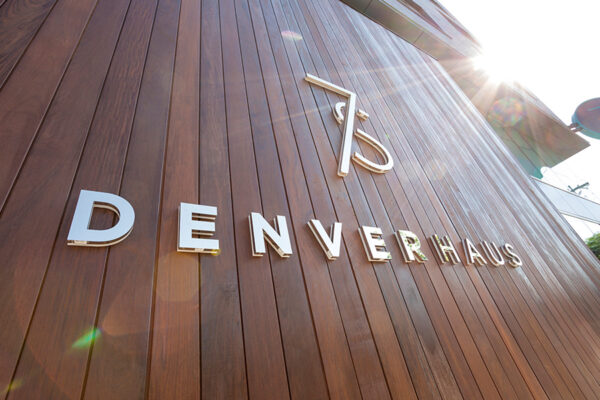 7 S Denver Haus metallic sign mounted on wood panel background.