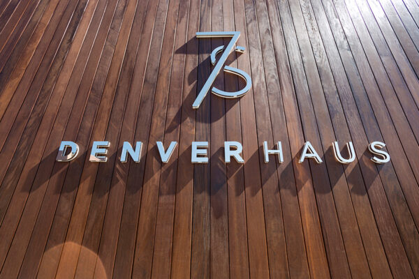 7 S Denver Haus metallic sign mounted on wood panel background.